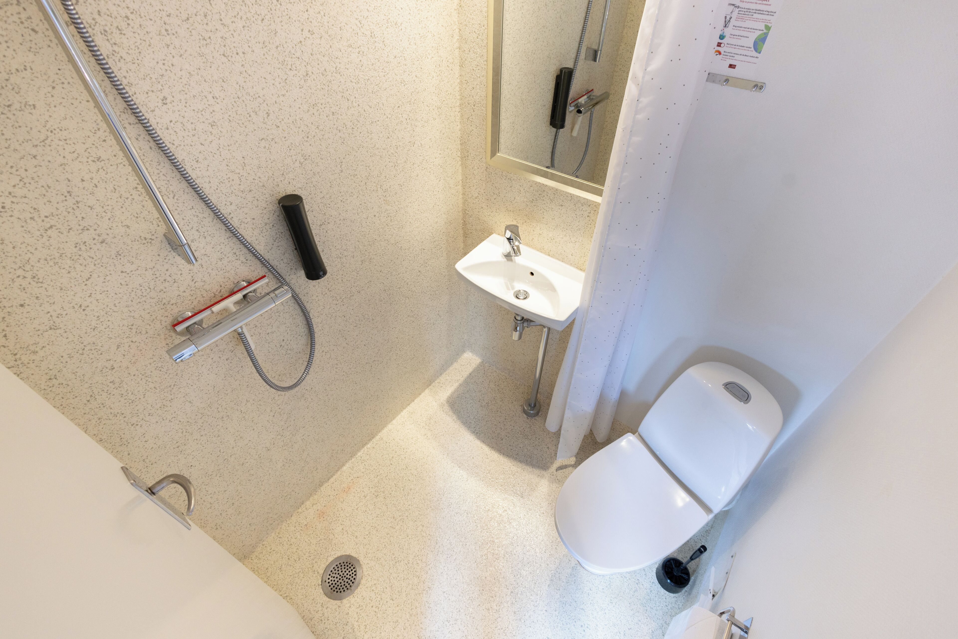 Et lille badeværelse med brusebad, håndvask og toilet.