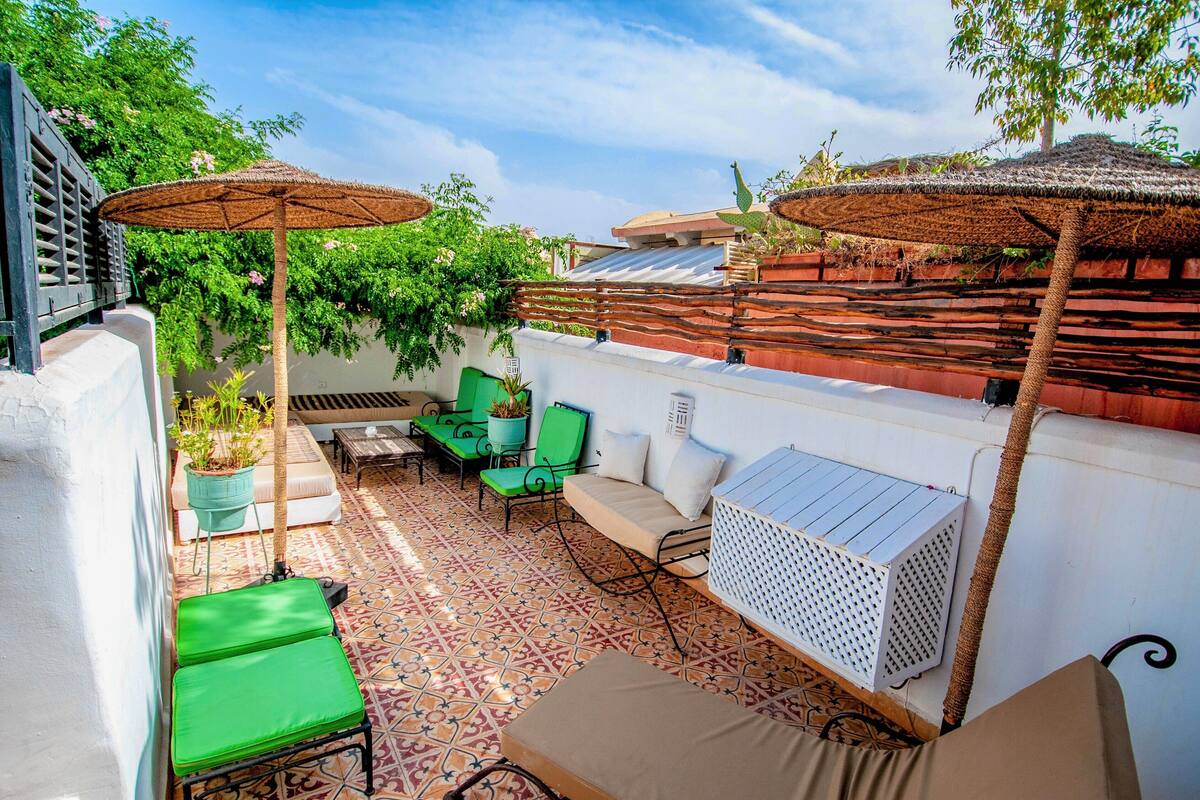 A patio with a patterned floor, green and beige seating, and a thatched umbrella.