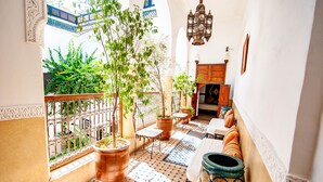A sunlit interior with a tiled floor, potted plants, a wooden bench, and a view of greenery outside.