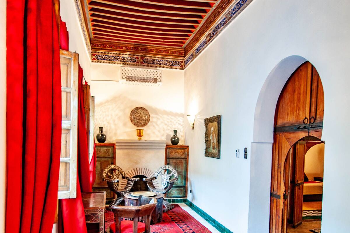 A room with a large bed, red curtains, a patterned rug, and traditional decor.
