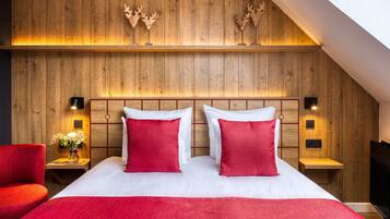 Hotelkamer met een houten hoofdeinde, twee rode kussens, een witte dekbedovertrek, een rode stoel en een klein tafeltje met een bloemenvaas.