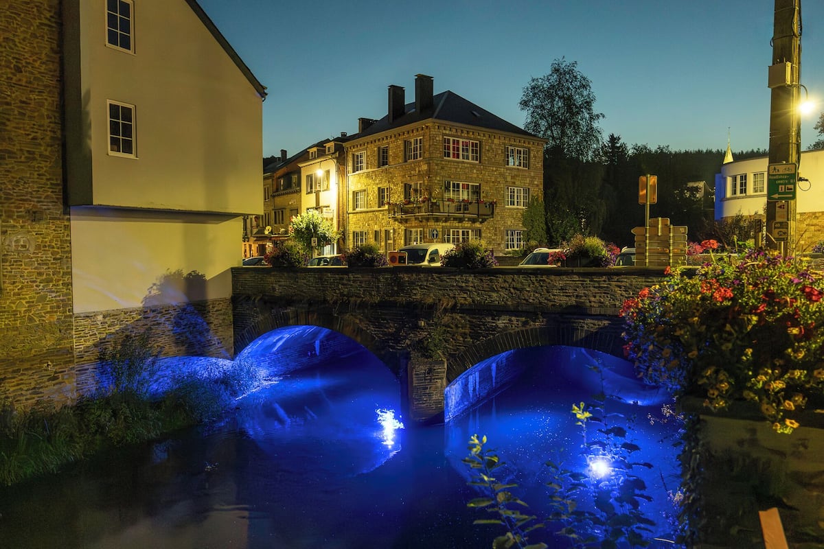 Un edificio histórico con fachada de piedra, un puente y un canal con luces azules iluminadas.