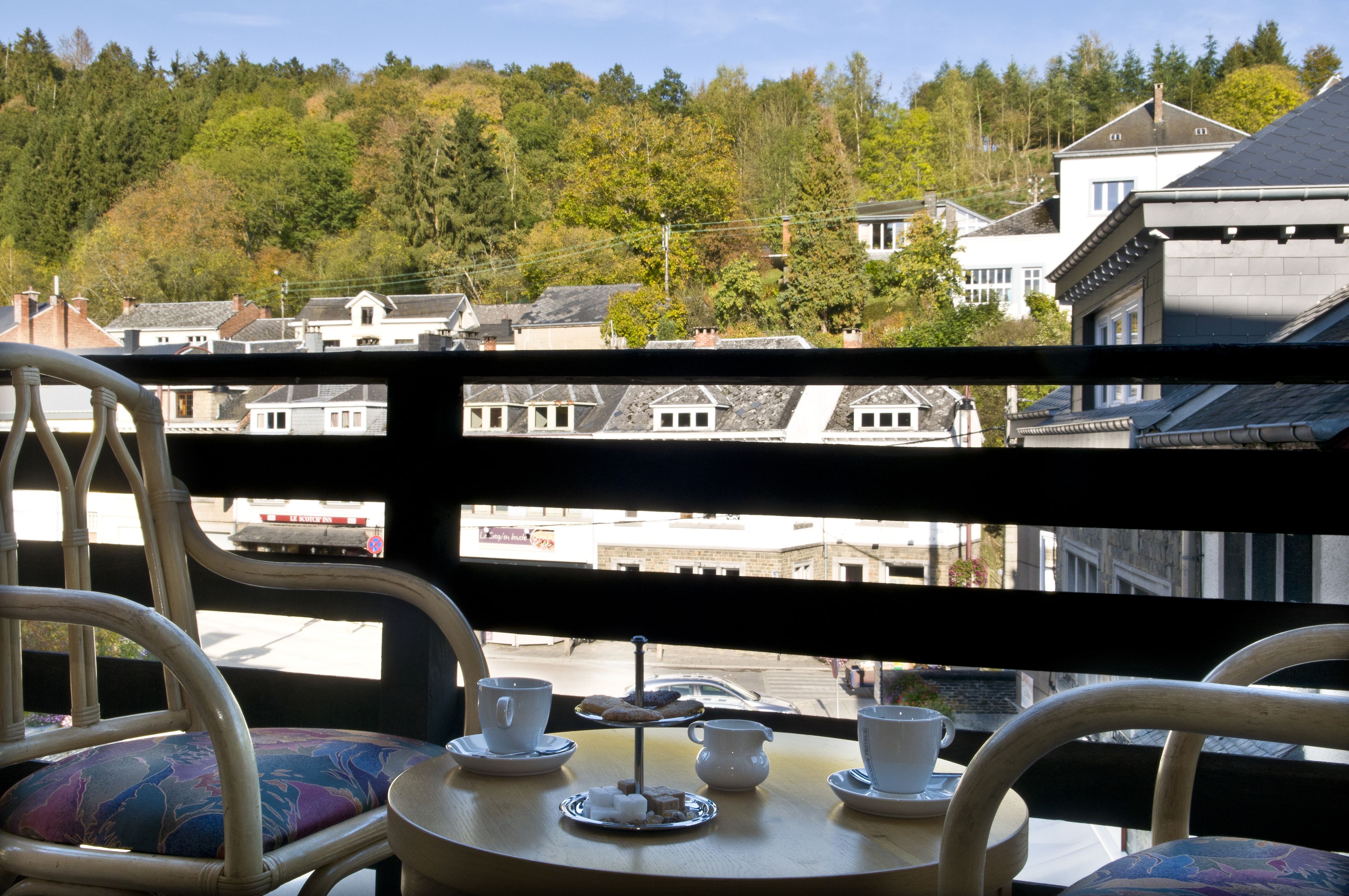 A balcony with a table set for tea, overlooking a residential area with houses and trees.