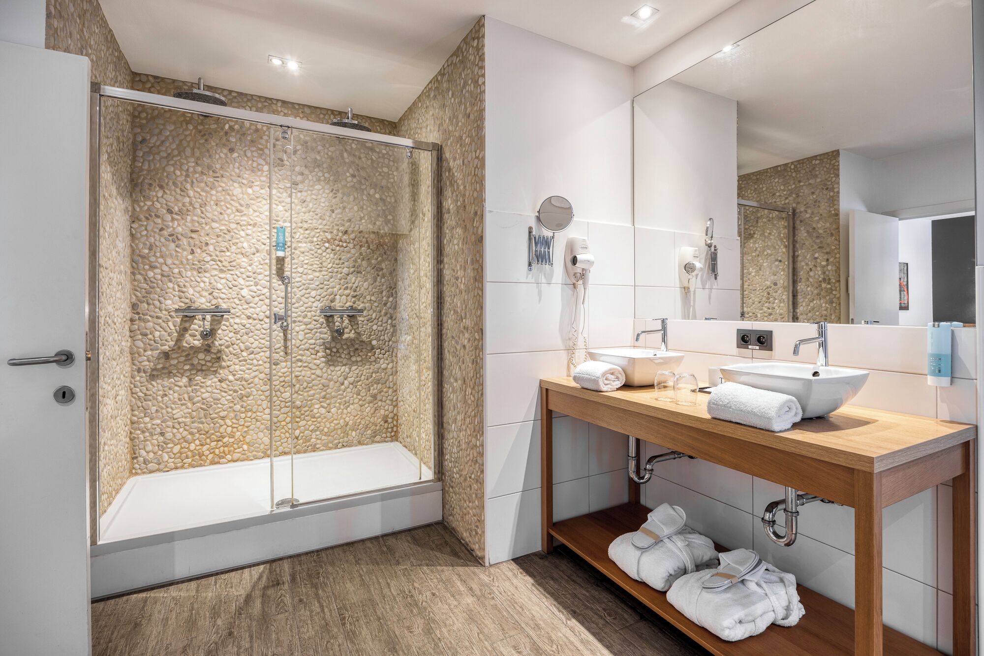 Un baño moderno con cabina de ducha de vidrio, tocador de madera con lavamanos y un espejo.