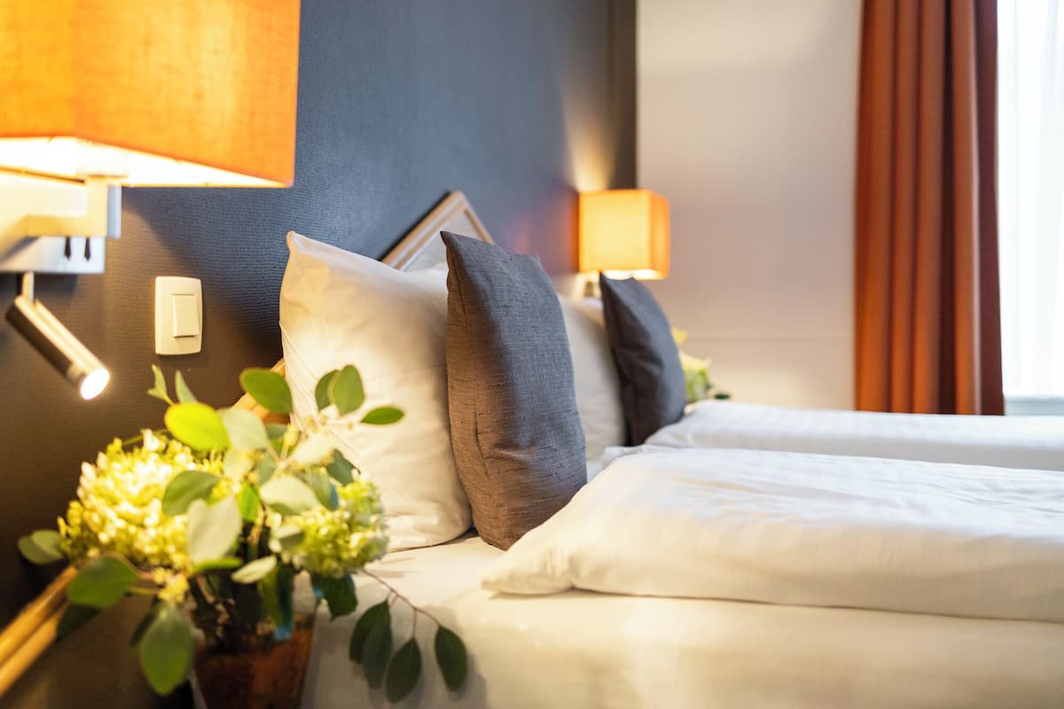 Habitación de hotel con dos camas, una mesita de noche con lámpara y una lámpara fijada a la pared.