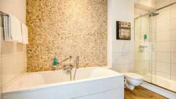 Un baño moderno con pared de guijarros, una bañera, un inodoro y una cabina de ducha de vidrio.