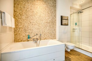 Un baño moderno con pared de guijarros, una bañera, un inodoro y una cabina de ducha de vidrio.
