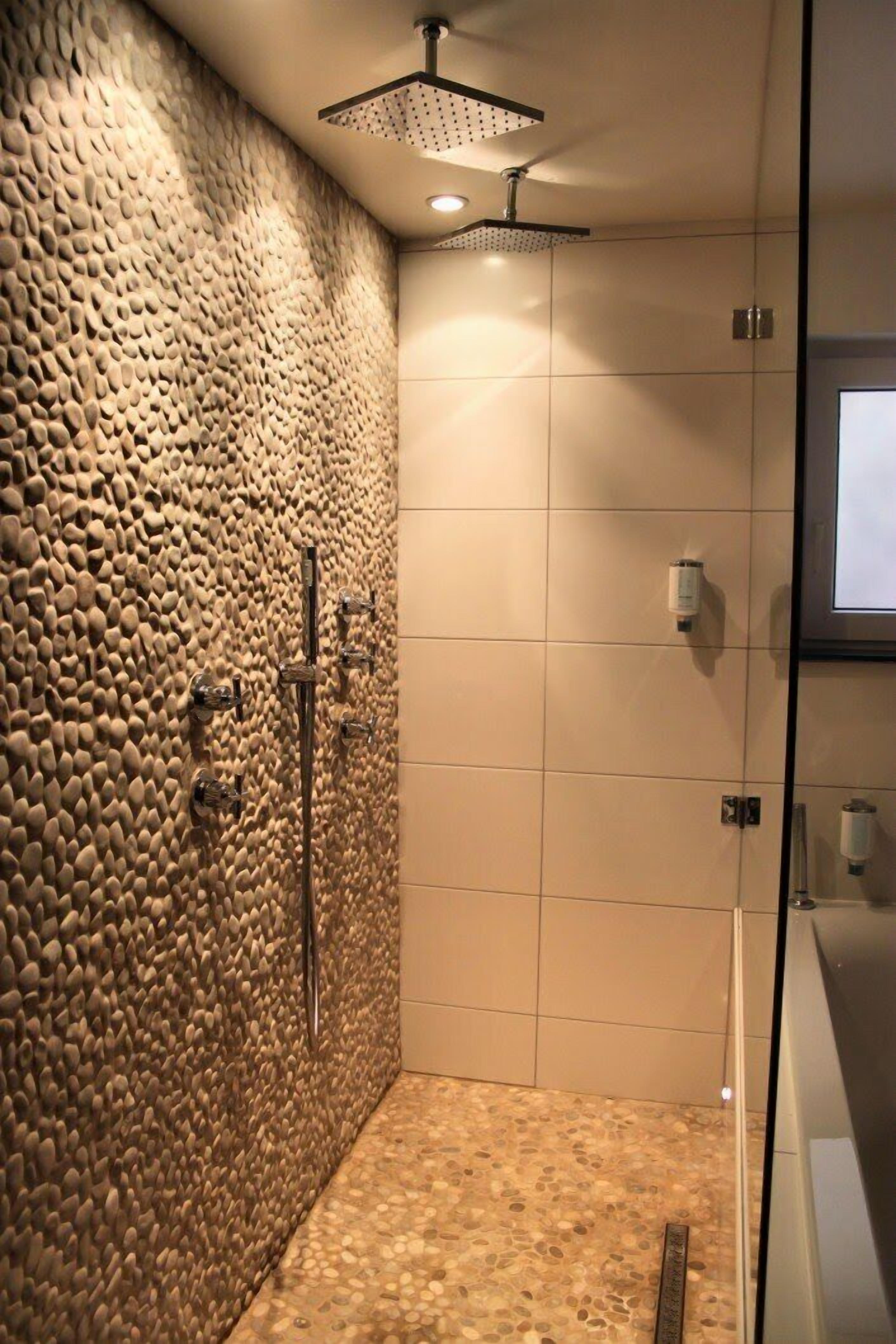 A modern shower with a pebble-textured wall, a glass door, and a tiled floor.