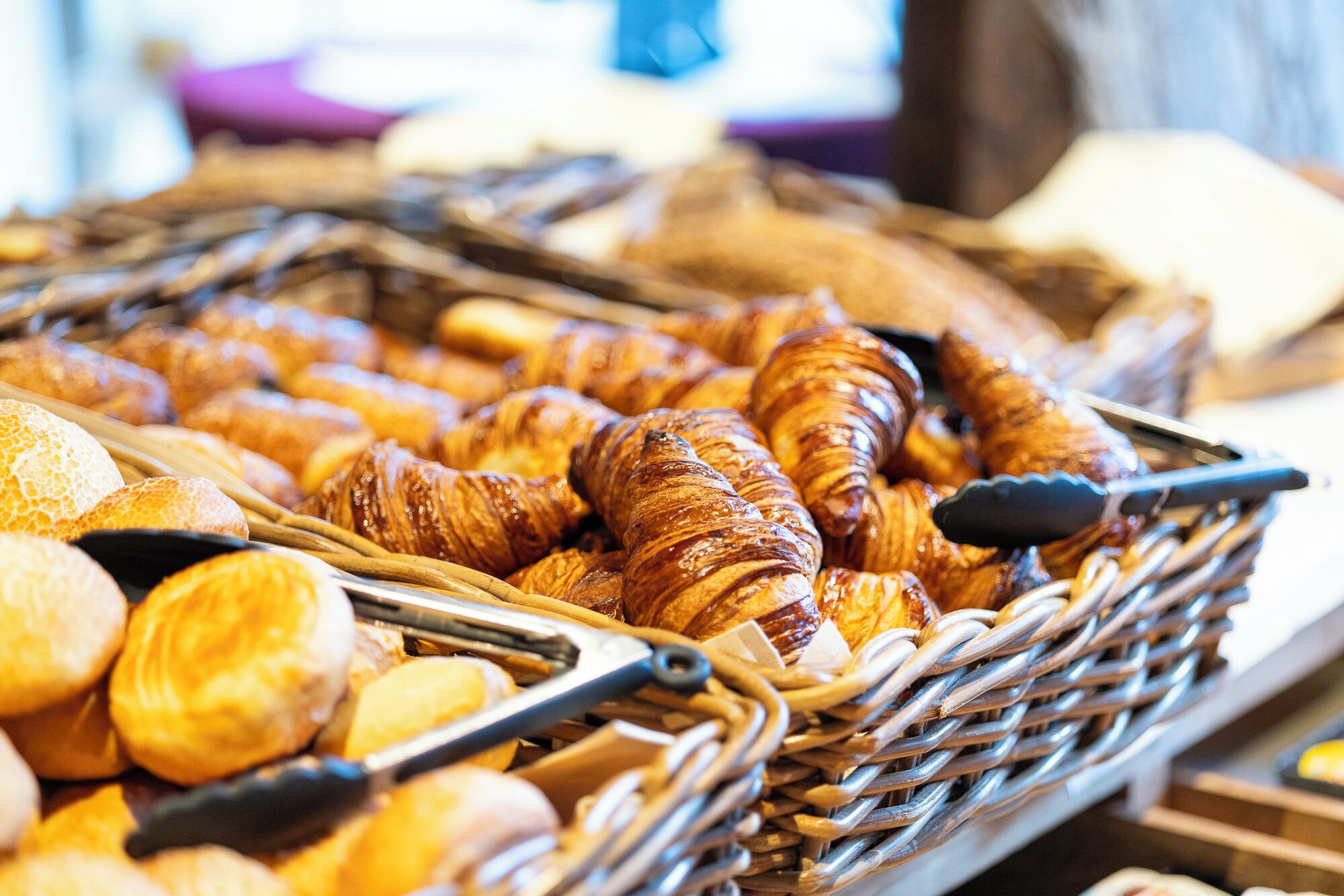 Un cesto pieno di dolci assortiti, tra cui croissant e panini.