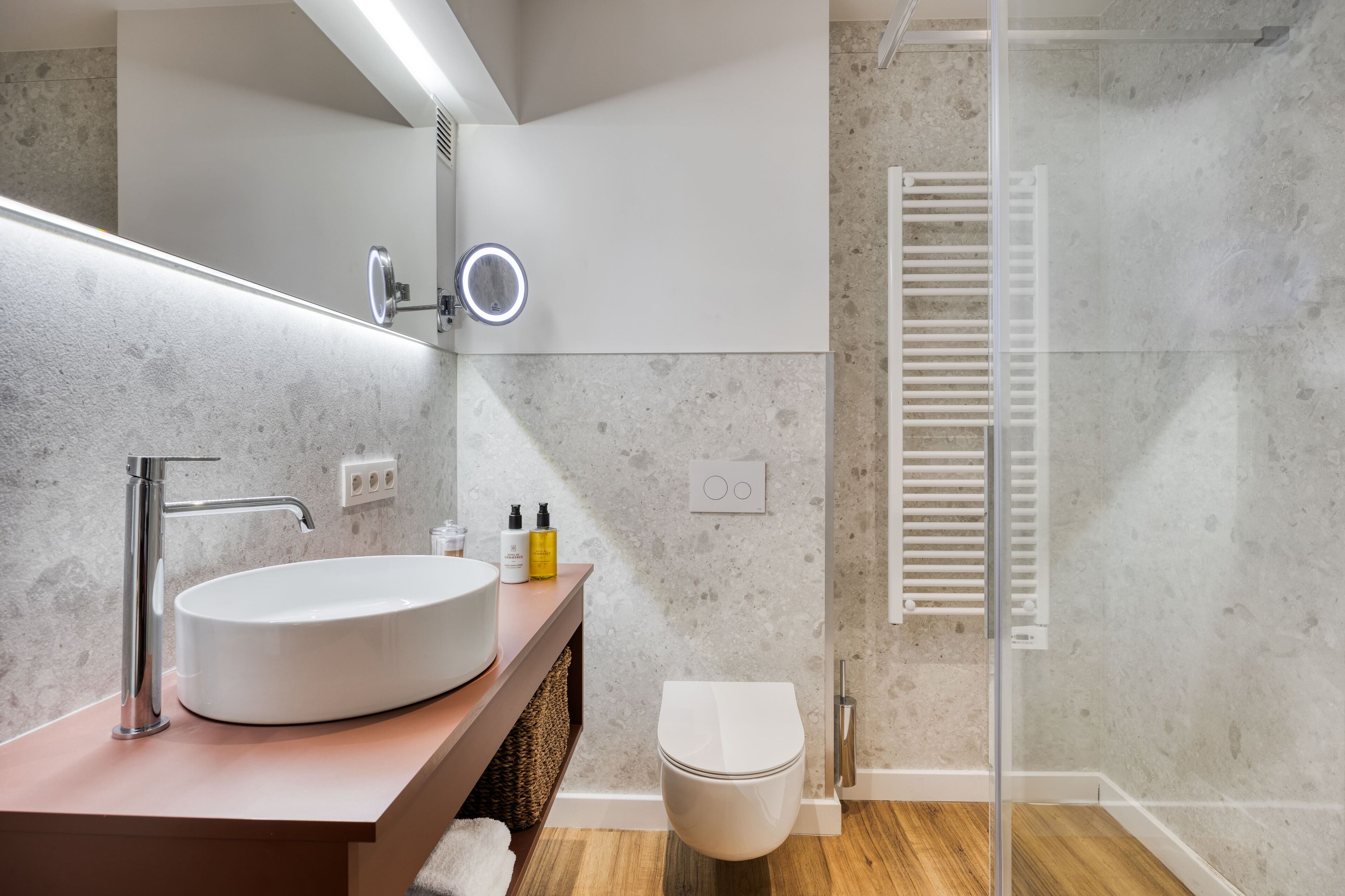Un baño moderno con un lavabo redondo, un espejo con iluminación, un inodoro y una cabina de ducha de vidrio.