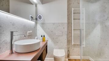 Un baño moderno con un lavabo redondo, un espejo con iluminación, un inodoro y una cabina de ducha de vidrio.
