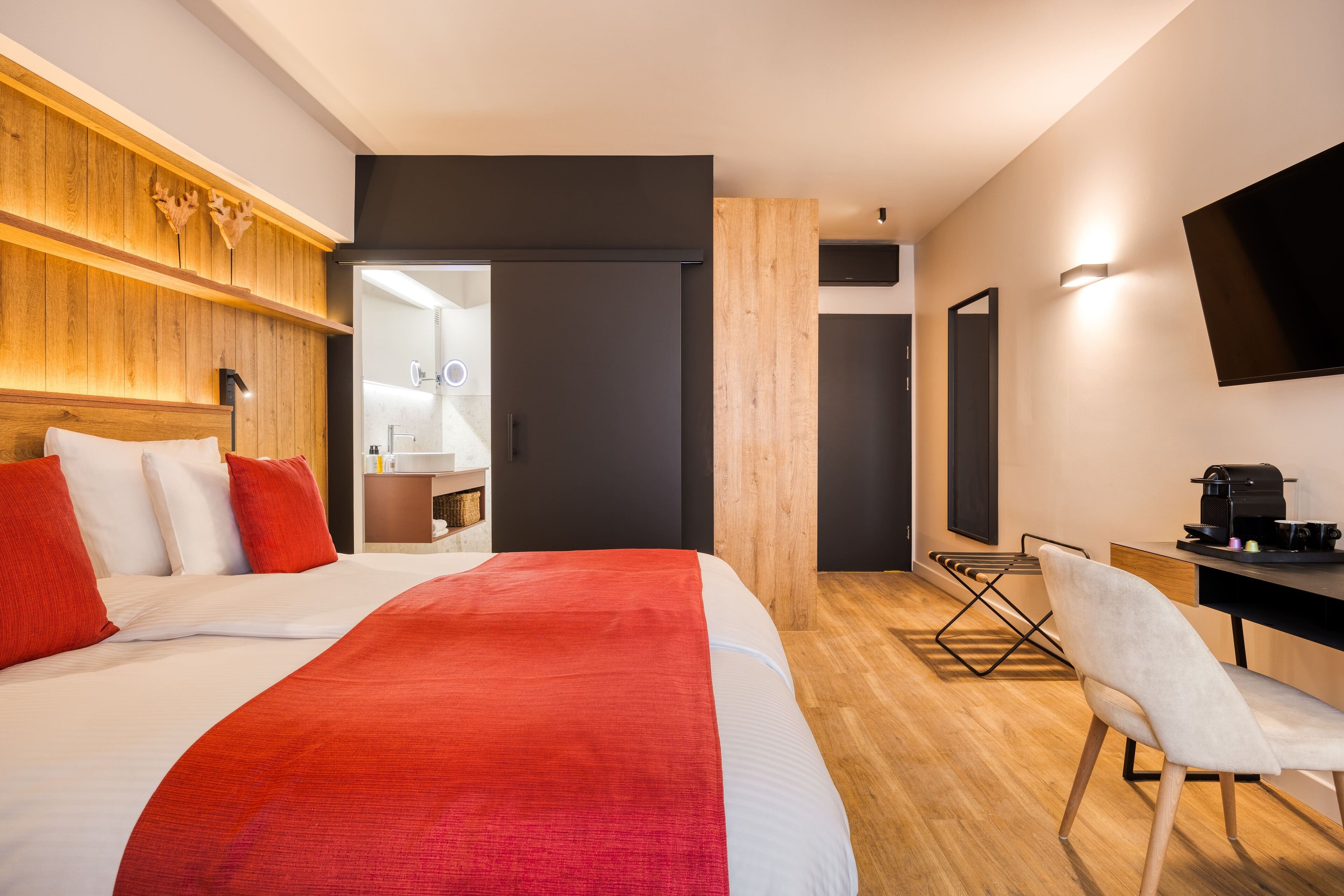 Een moderne hotelkamer met een groot bed, een bureau, een stoel en een aan de muur bevestigde televisie.