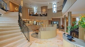 A spacious lobby with a marble staircase, a reception desk, and a seating area with tables and chairs. - Hotel Quartier Latin (Marche-en-Famenne)