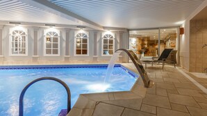 An indoor swimming pool with a waterfall feature, surrounded by a tiled deck and a glass entrance to a spa area. - Hotel Quartier Latin (Marche-en-Famenne)