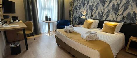 Quarto de hotel com cama, escrivaninha, cadeira, mesinha e lixeira.