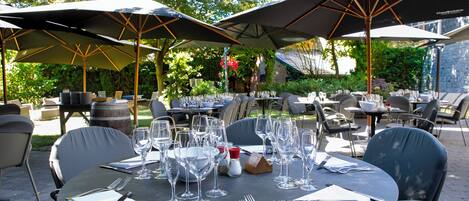 An outdoor dining area with round tables, chairs, and large umbrellas.