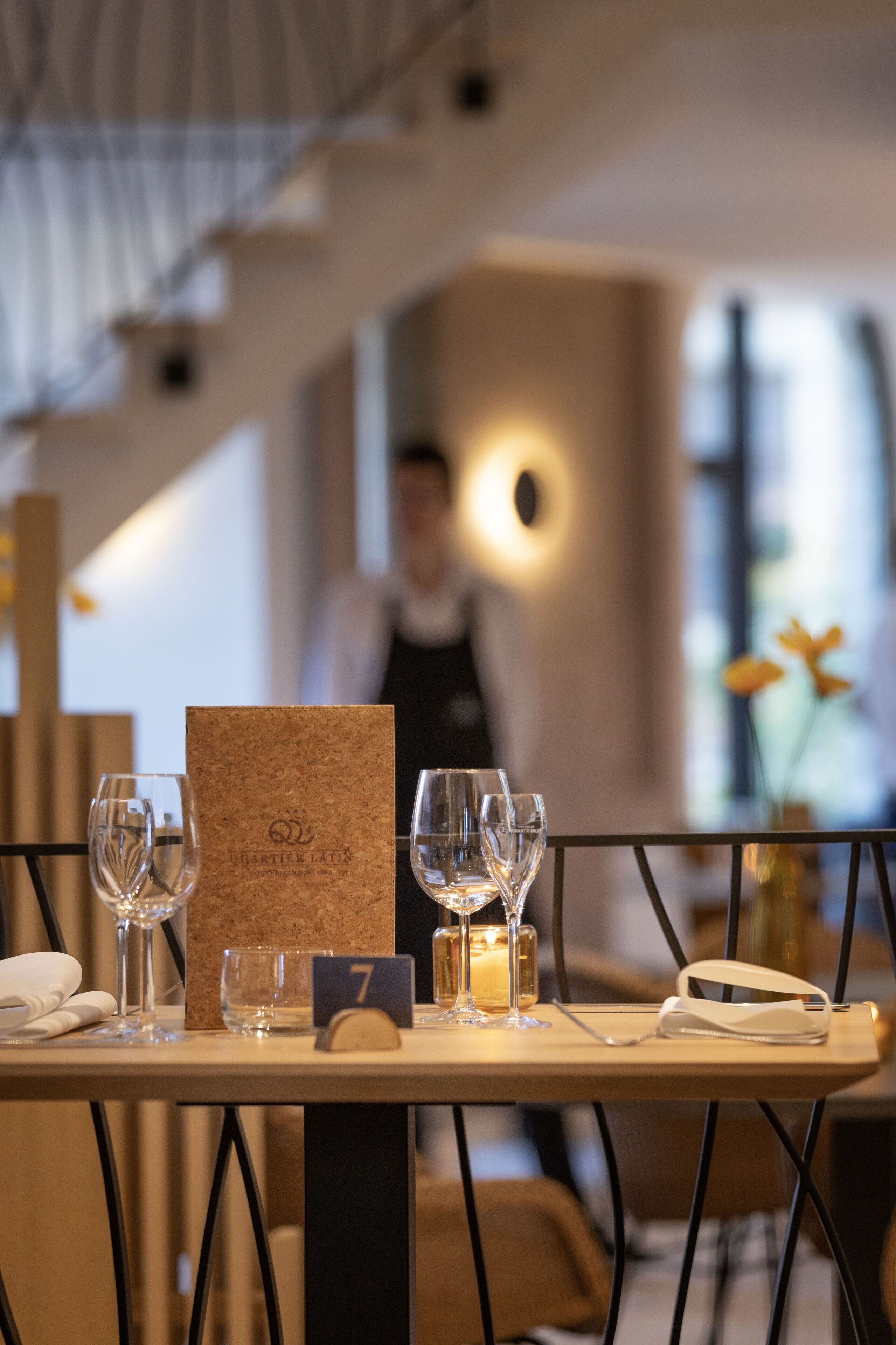 Une table de restaurant avec un menu en liège, des verres numérotés et une bougie.