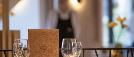 Una mesa de restaurante con una carta de corcho, copas numeradas y una vela.