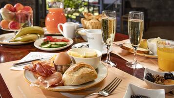 Une table de petit-déjeuner avec des croissants, du bacon, des œufs et des fruits. On y trouve également deux verres de champagne et une carafe de jus d’orange.