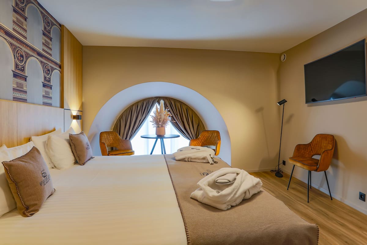 A hotel room with a large bed, two armchairs, a small table, and a TV.