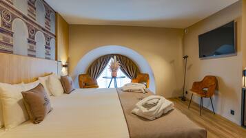 A hotel room with a large bed, two armchairs, a small table, and a TV.