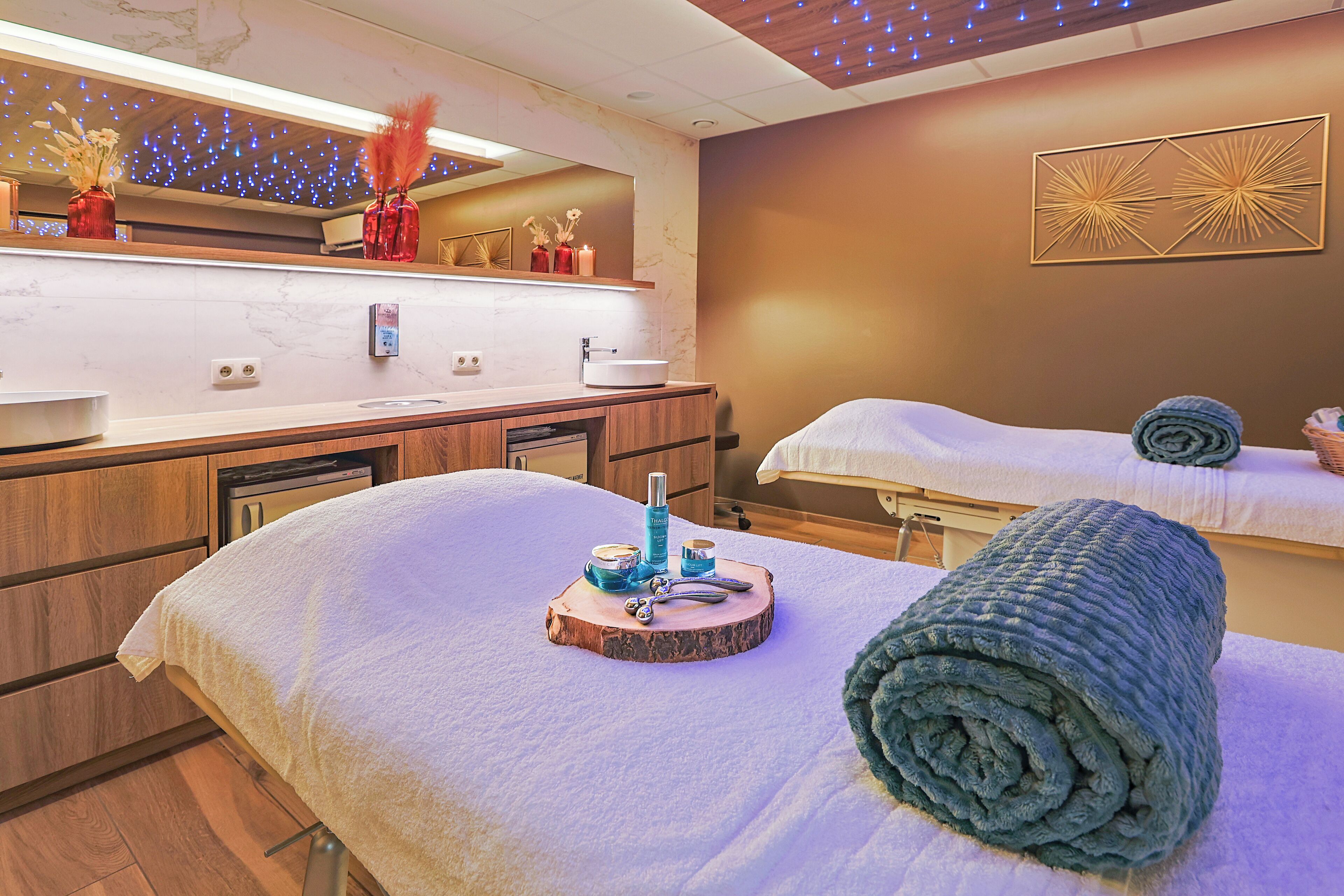 A spa room with a wooden vanity, a mirror, and a bed with towels and a bathrobe.