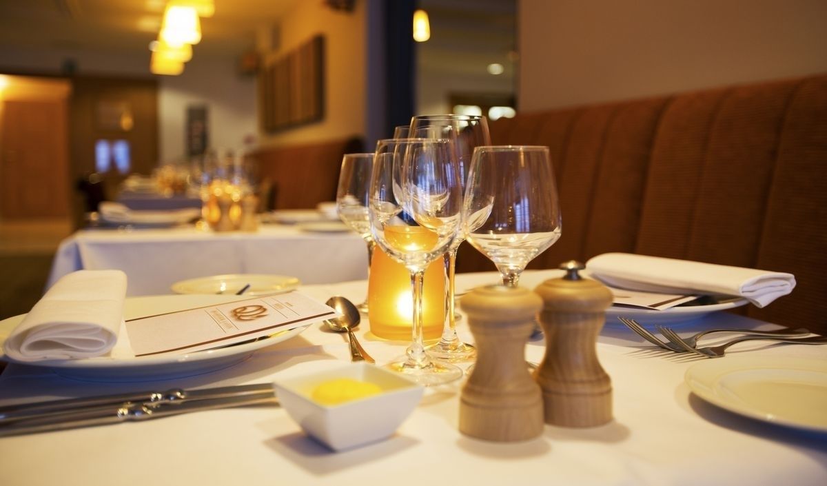 A restaurant table set with wine glasses, a candle, salt and pepper shakers, a bowl of lemon, and a menu.