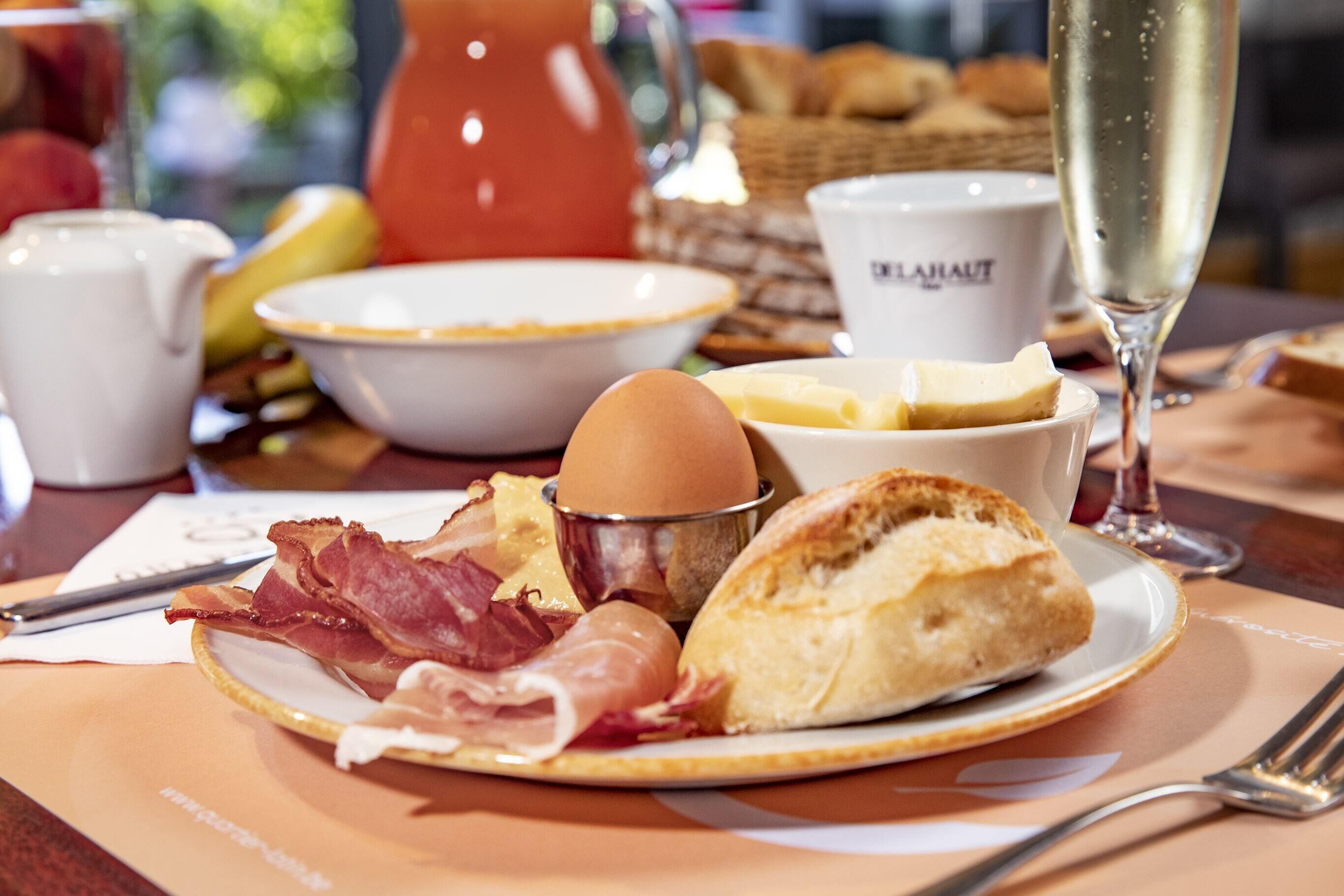 A breakfast setting with a plate of eggs, bacon, and pastries, a glass of champagne, and a coffee cup.