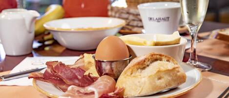 A breakfast setting with a plate of eggs, bacon, and pastries, a glass of champagne, and a coffee cup.