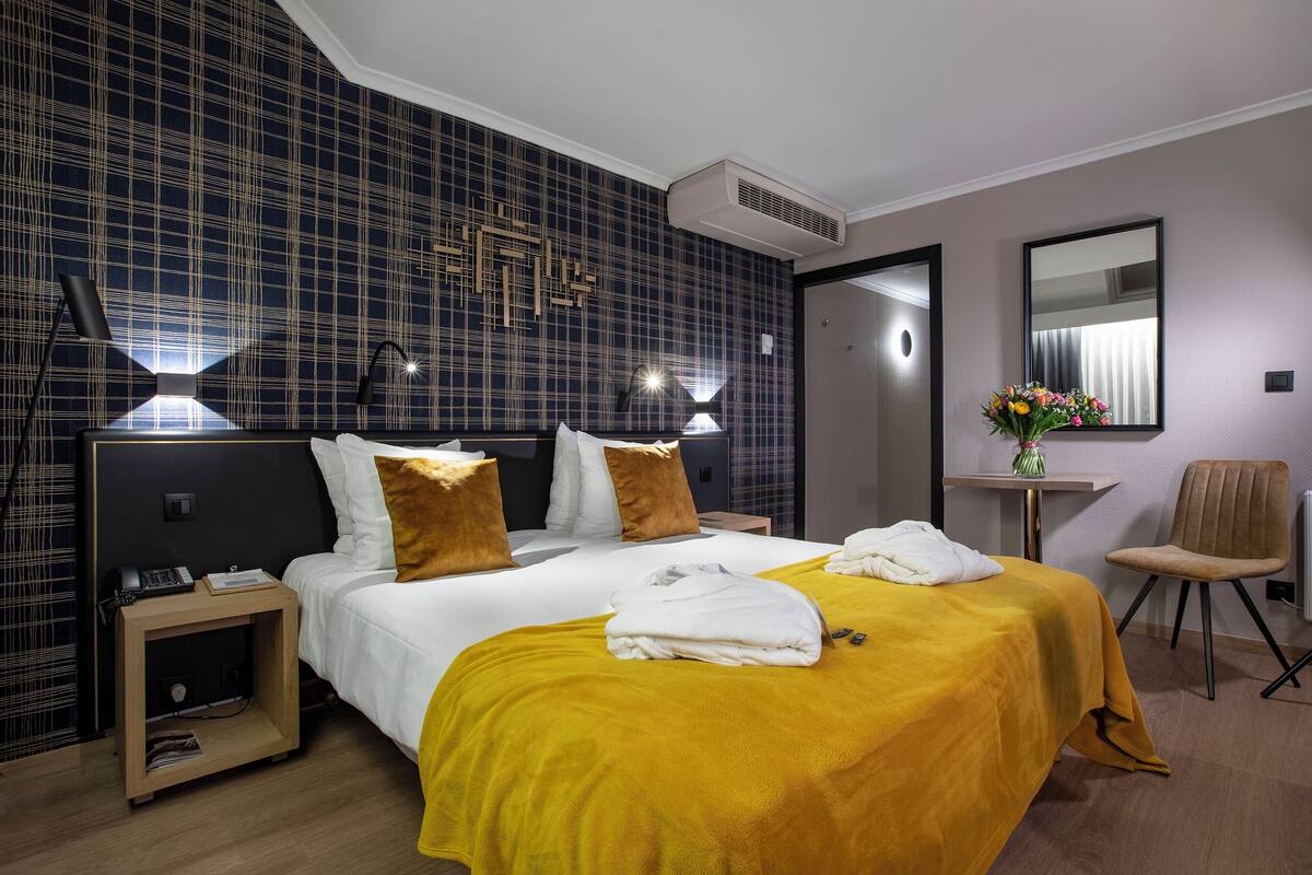 A hotel room with a large bed, a bedside table, a chair, and a small table with a vase of flowers.