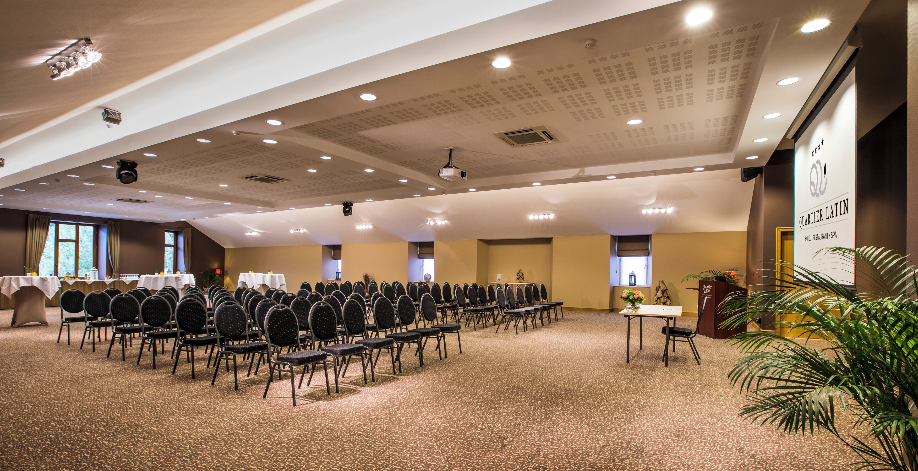 A conference room with rows of chairs, tables, and ceiling lights.