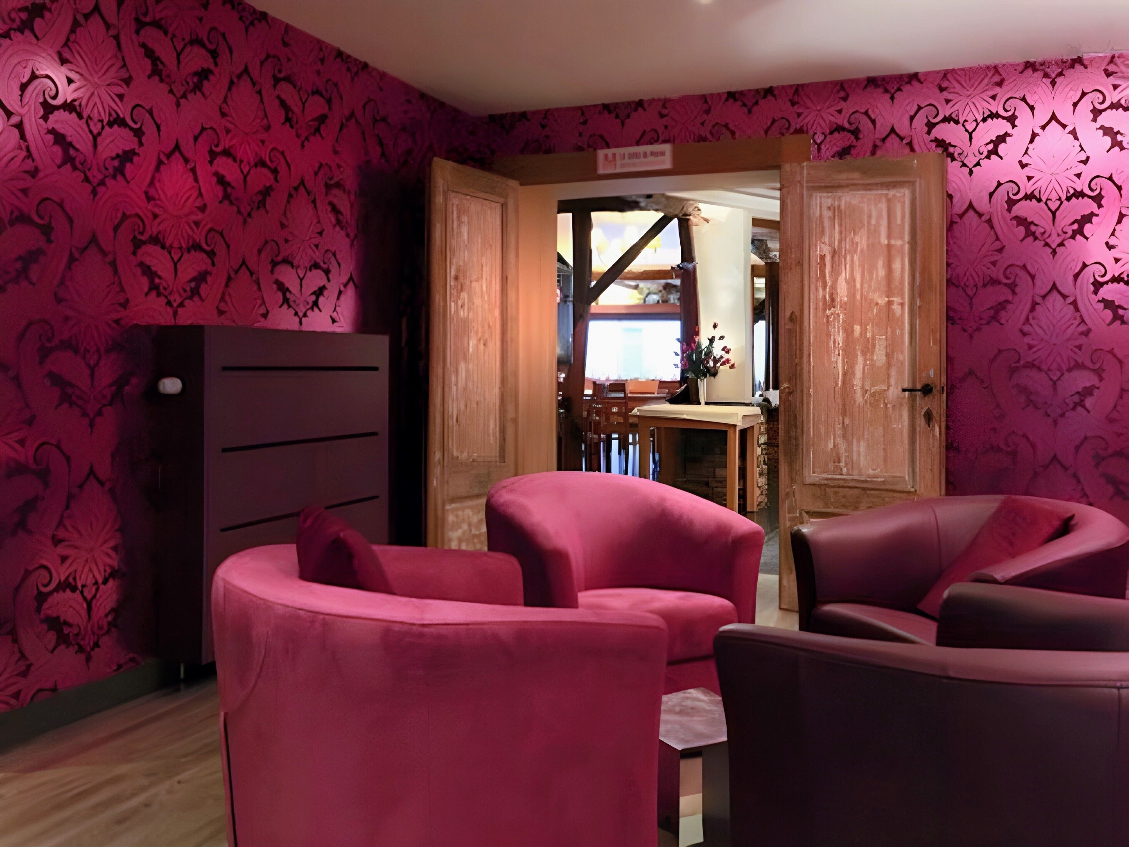 Una habitación con papel tapiz estampado en rosa, un armario de madera y dos sillones rosados.