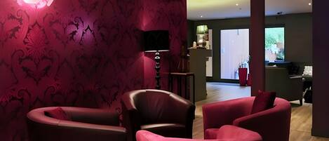 A modern living room with dark red patterned wallpaper, leather sofas, and a flat-screen TV mounted on the wall.
