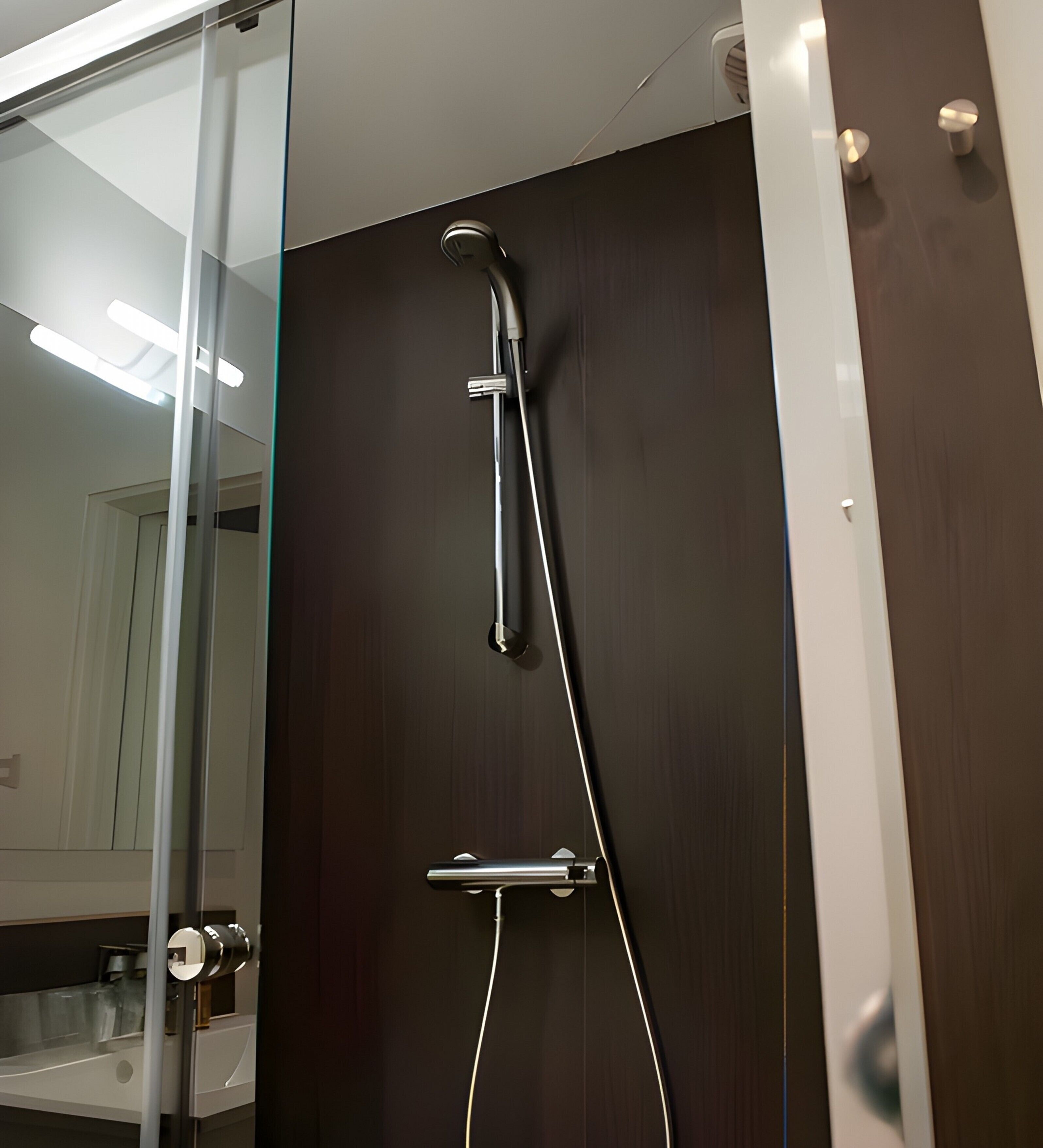Una doccia moderna con cabina in vetro, porta in legno scuro e un mobile bagno con accessori.