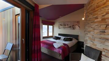 A bedroom with a bed, a chair, a window, and a wall with a stone-like texture.
