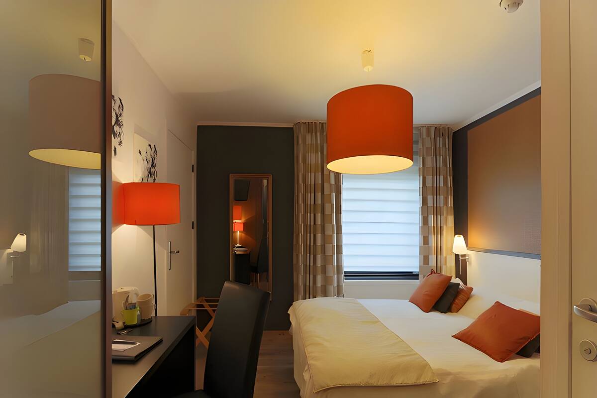 A hotel room with a bed, desk, chair, and two lamps.