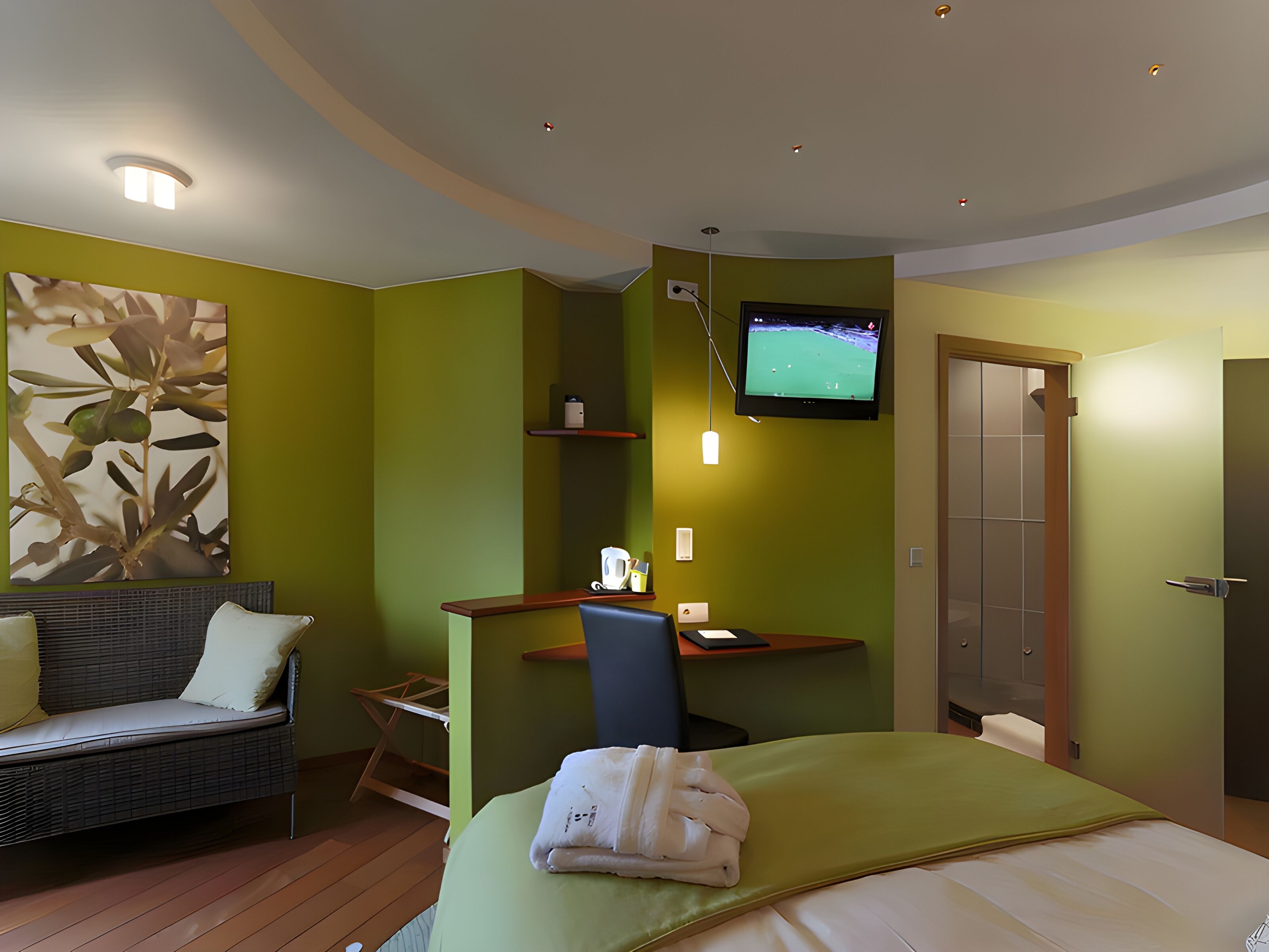 Ein Hotelzimmer mit Bett, Schreibtisch mit Stuhl, Fernseher, Sofa und einer Wandablage.