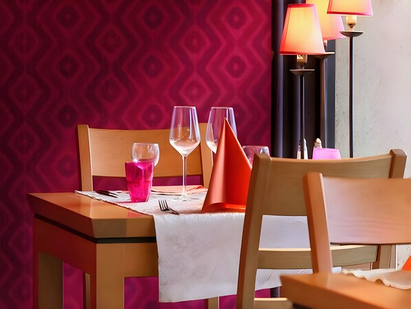 Una mesa servida con mantel blanco, dos copas de vino, un vaso rosa y una servilleta roja.