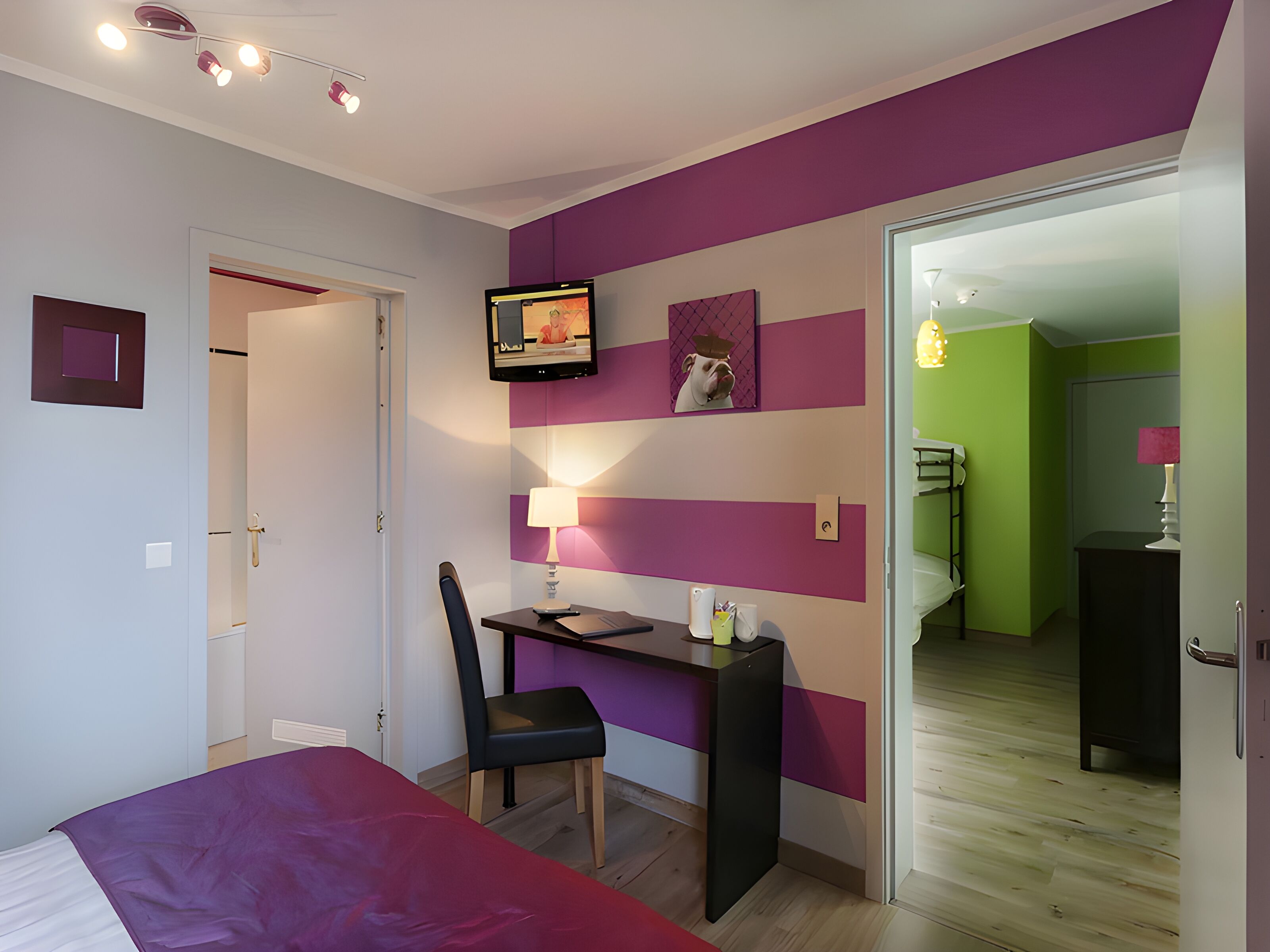 A bedroom with a bed, desk, chair, and a TV mounted on the wall.