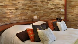 Un dormitorio con pared de piedra, una cama con muchos almohadones y una mesita de noche con un dispensador de pañuelos.