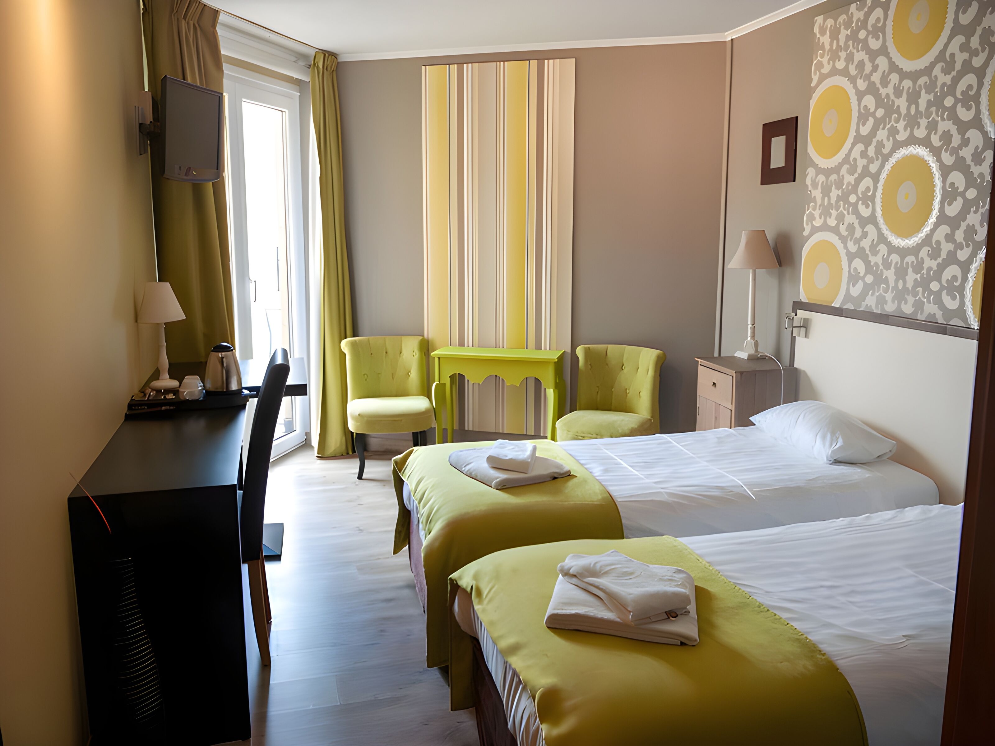 Een hotelkamer met twee bedden, een bureau, een stoel, een televisie en een kamer met een patroon op de muur.
