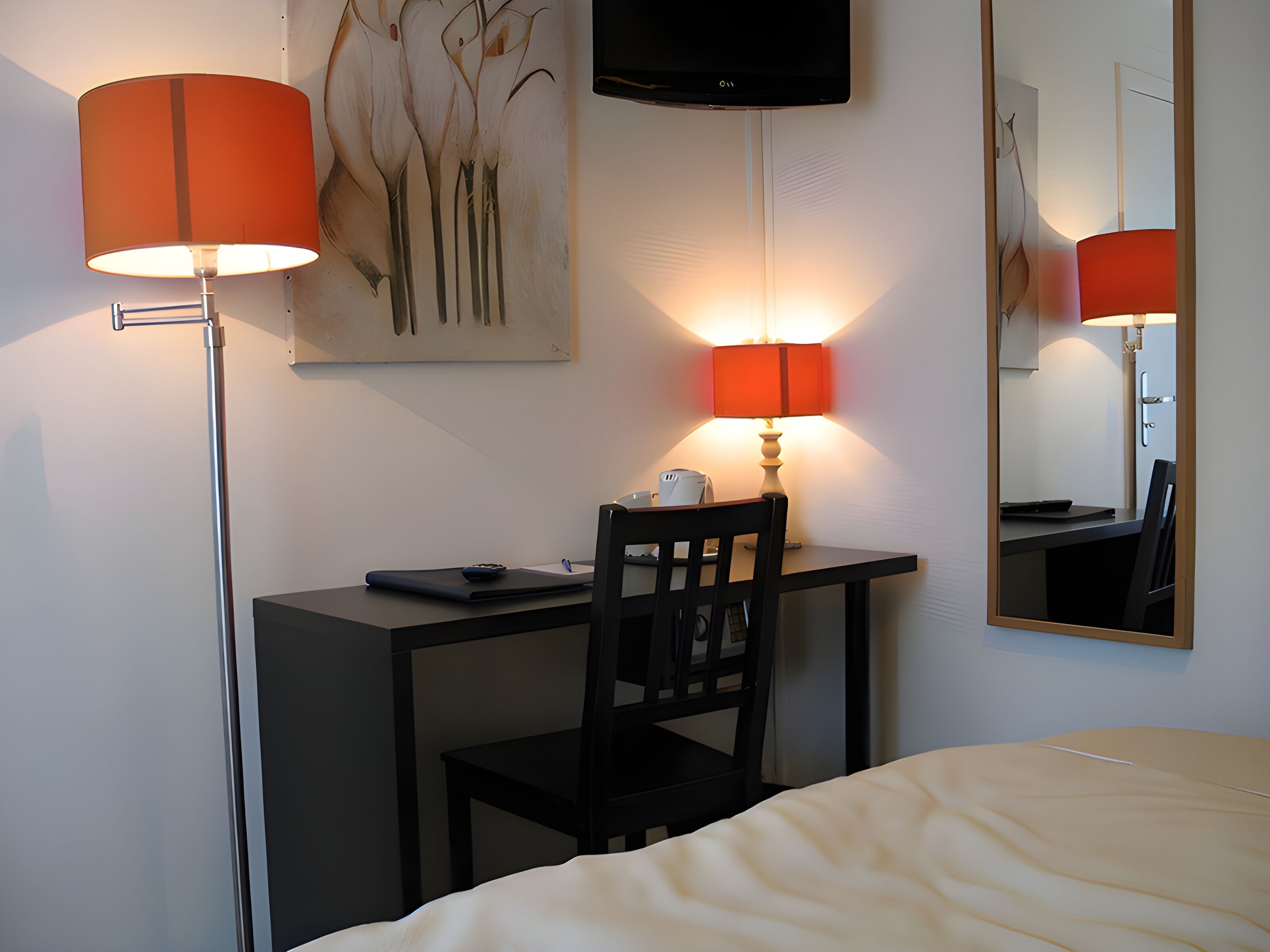 Quarto de hotel com escrivaninha, cadeira, cama e televisão de tela plana presa na parede.