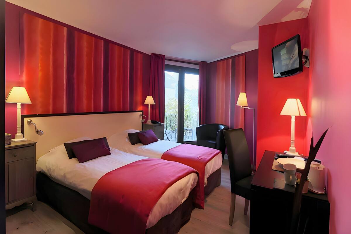 A hotel room with two beds, a desk, a chair, a TV, and a balcony with a view.