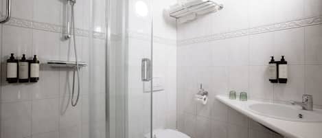 A modern bathroom with a glass-enclosed shower, a toilet, a sink with hand soap, and shampoo bottles.