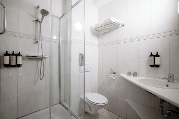 Un baño moderno con ducha de vidrio, inodoro, lavamanos con jabón de manos y botellas de champú.