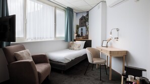 Hotelkamer met een bed, bureau, stoel, televisie en raam met gordijnen.