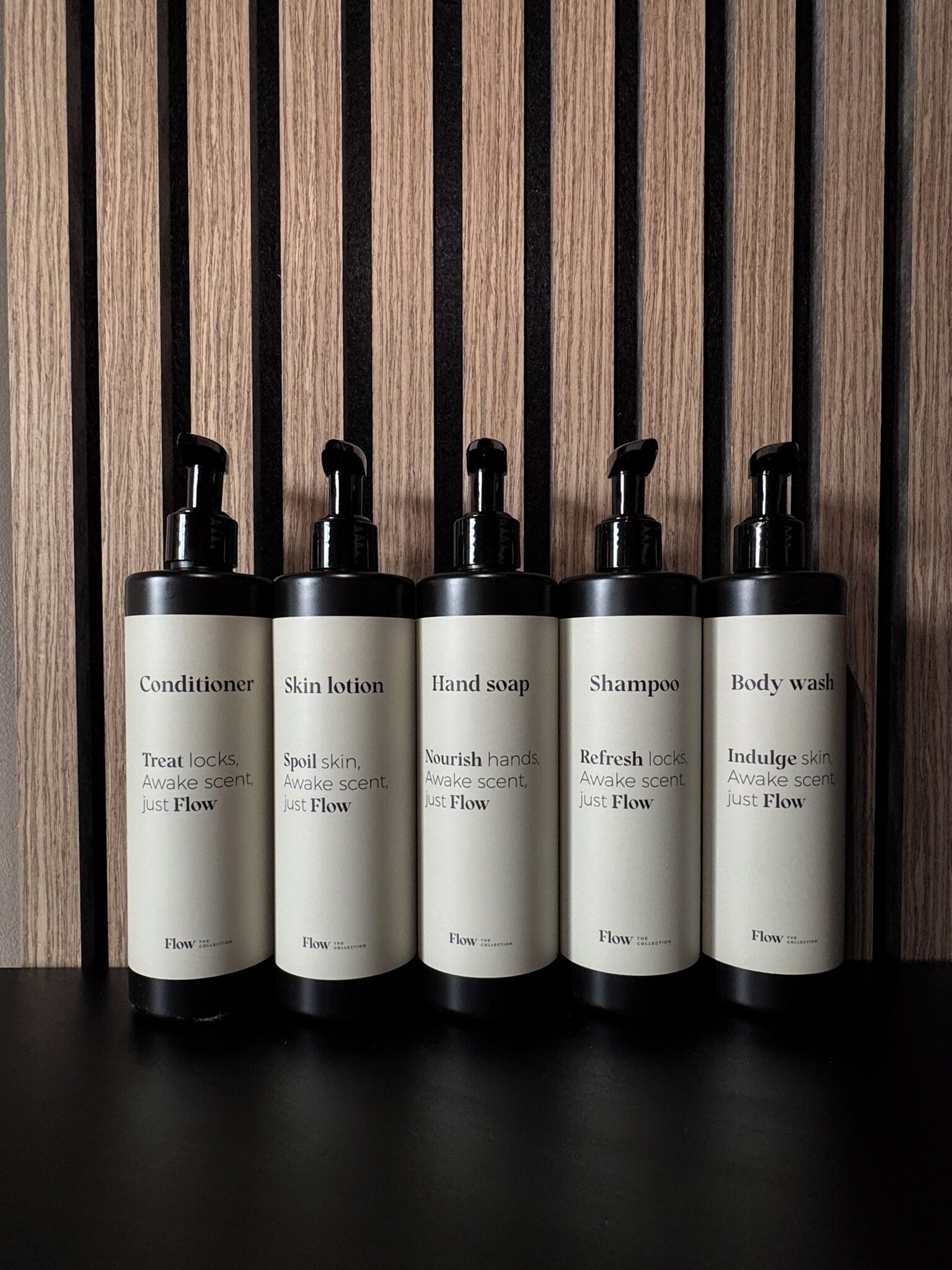 Cinco botellas de productos para el cuidado de la piel con la etiqueta 'Flow' sobre un fondo de madera.