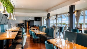 Een restaurant met houten tafels en stoelen, een klok aan de muur en grote ramen met uitzicht op het water.