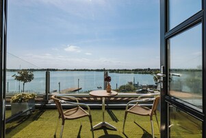 A room with a view of a lake, two wicker chairs, a small round table, and a vase with flowers.