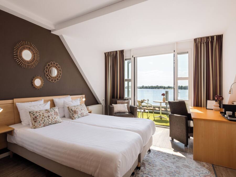 Een hotelkamer met een groot bed, een bureau en uitzicht op het water.